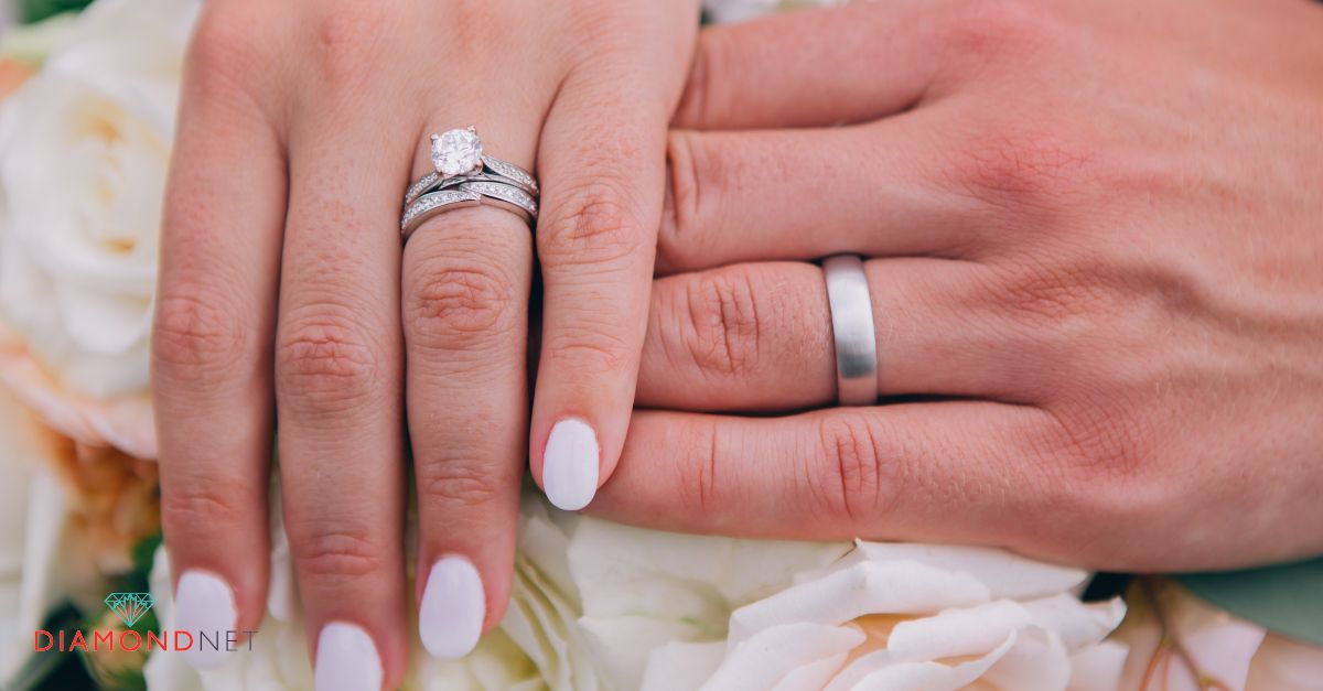 A bride and groom holding hands, showcasing their wedding rings on their ring fingers.