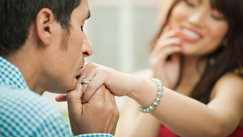 Young man kissing his girlfriend hand with engagement ring