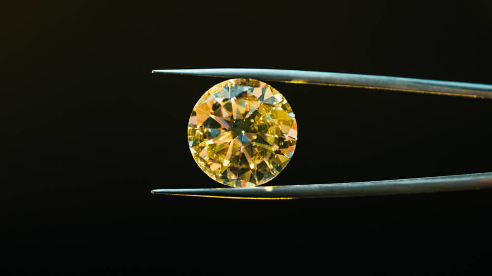 Colorful yellow sparkling diamond in tweezers