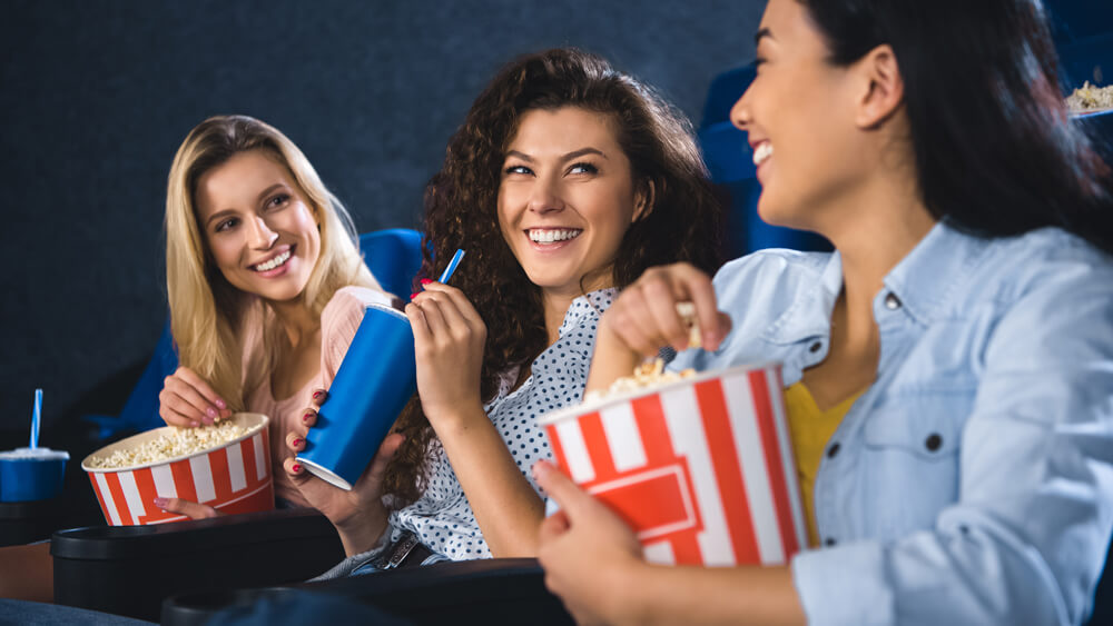 Happy multiracial women with popcorn watching film