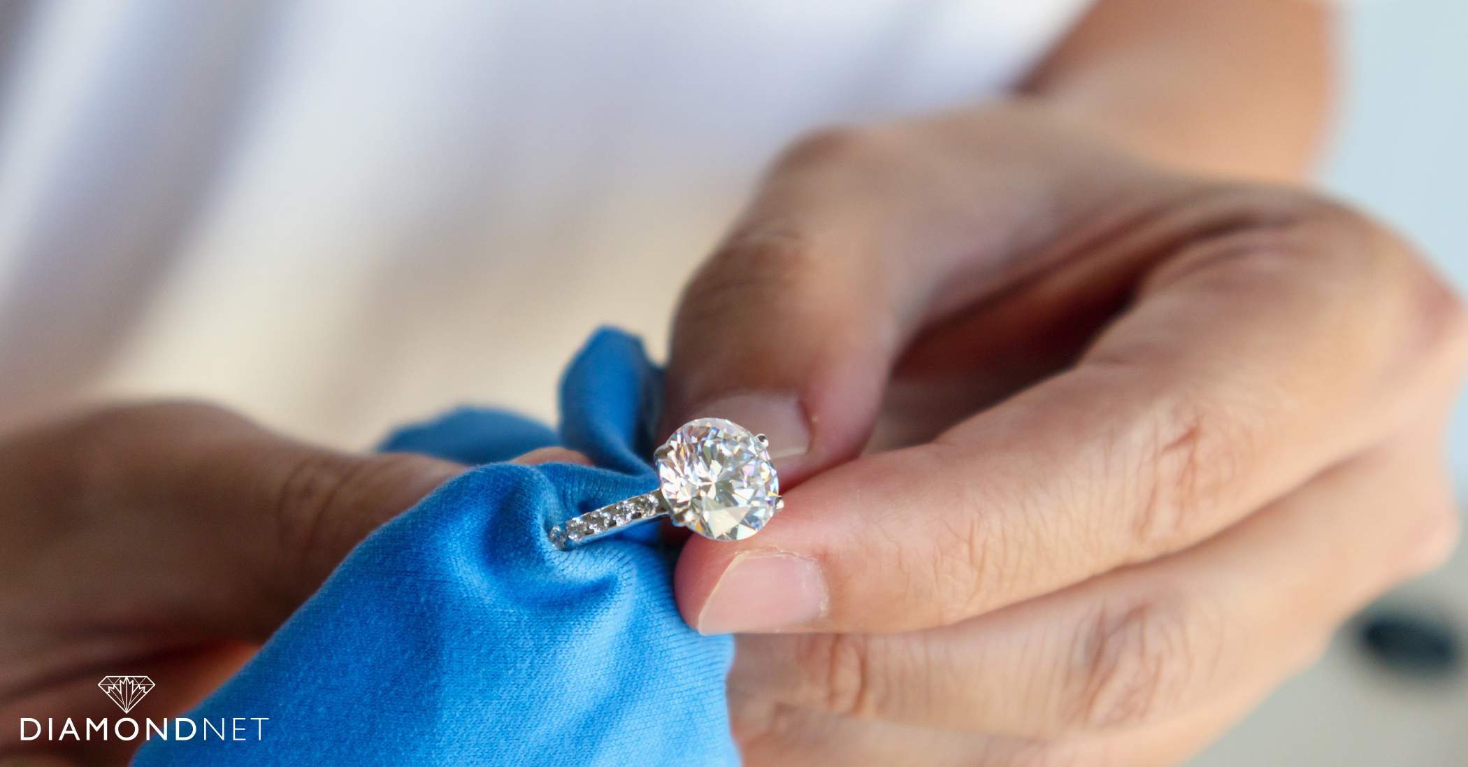 An individual uses a cloth to polish an engagement ring, highlighting proper gemstone care and maintenance techniques.