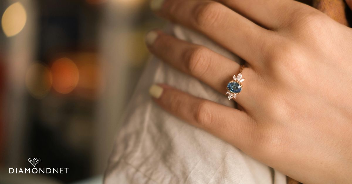 A woman's hand holds a gold ring featuring a blue sapphire, showcasing a lab-grown gemstone design